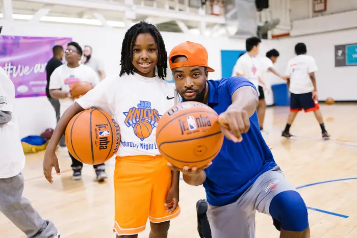 A young girl and a man posing together on a basketball court, smiling.